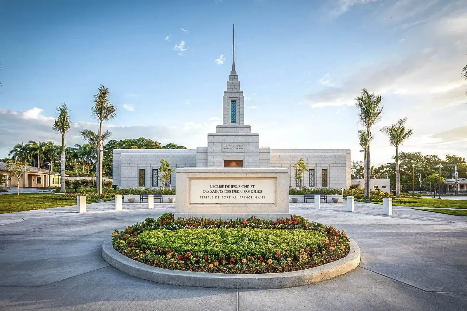 Front of the temple with its name sign on a stone monument and a round flower bed.