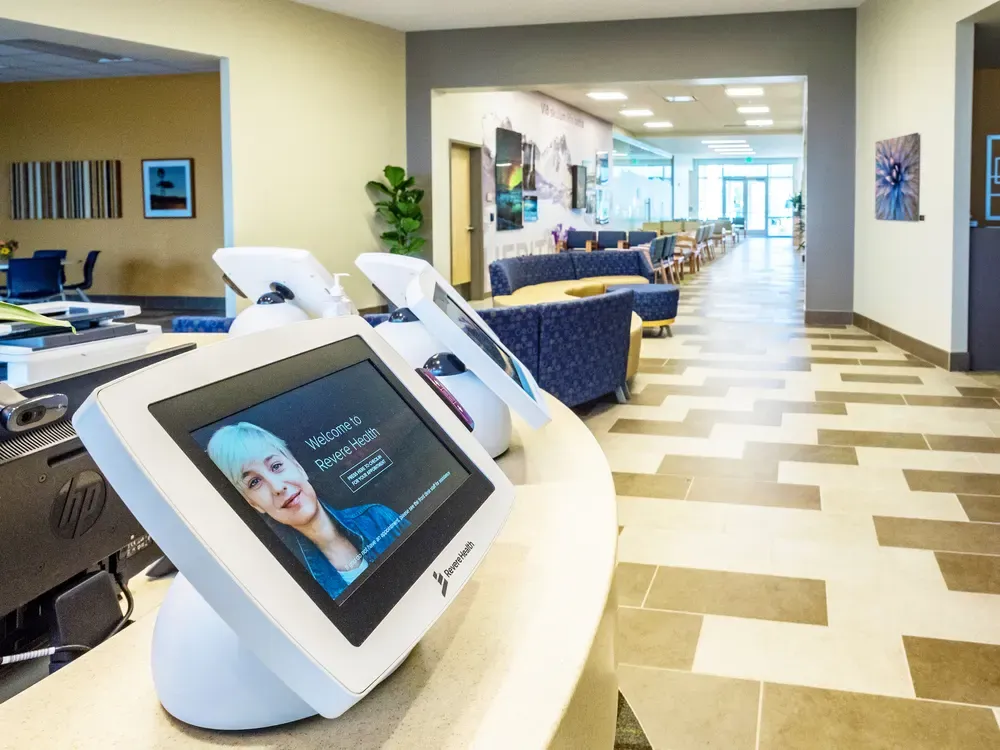 Check-in kiosk screens on a curved counter, with a long tiled lobby beyond.