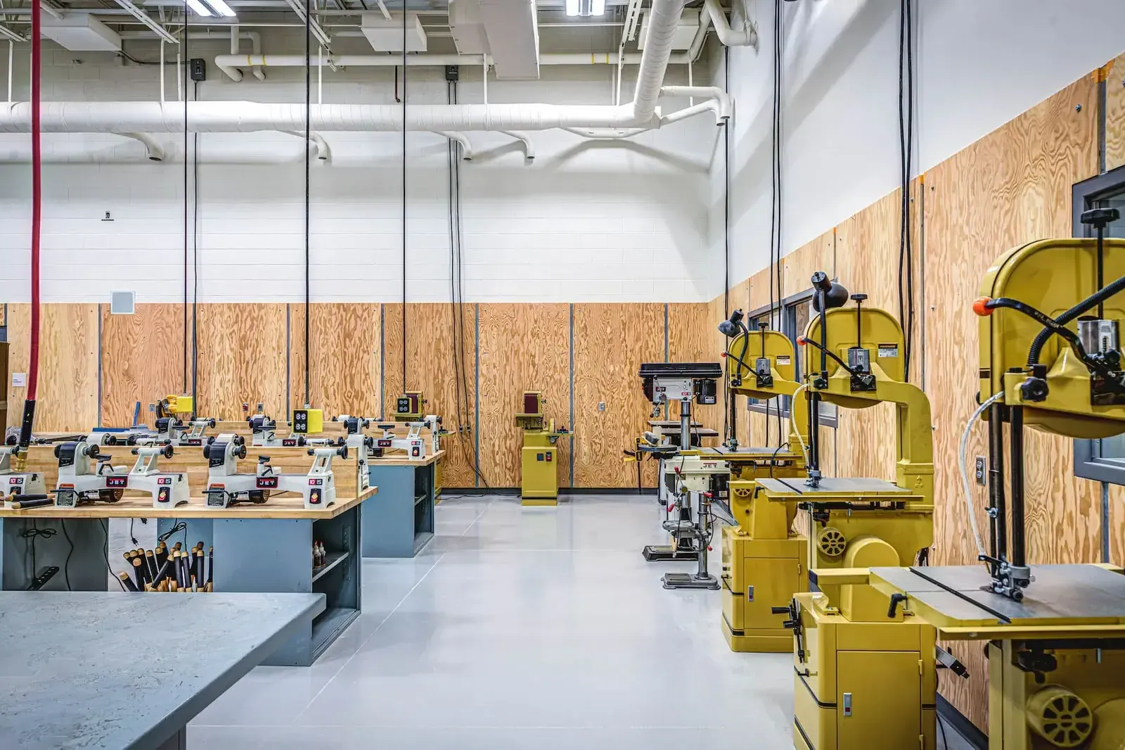 Woodshop with workbenches, band saws, and plywood-lined walls.