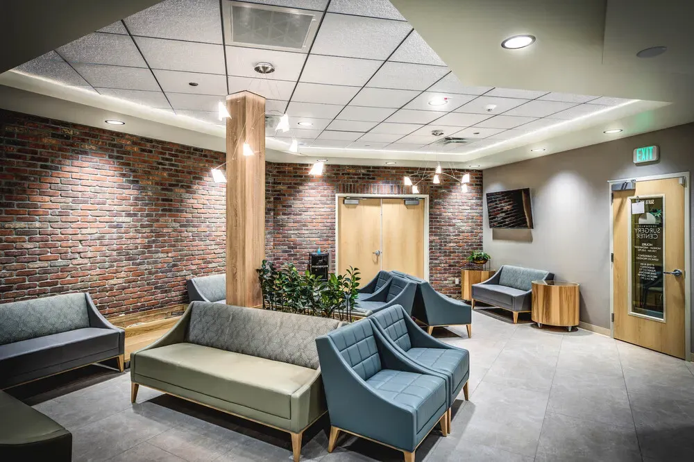 Waiting room with a brick wall, a wood column, and teal and gray armchairs and sofas.