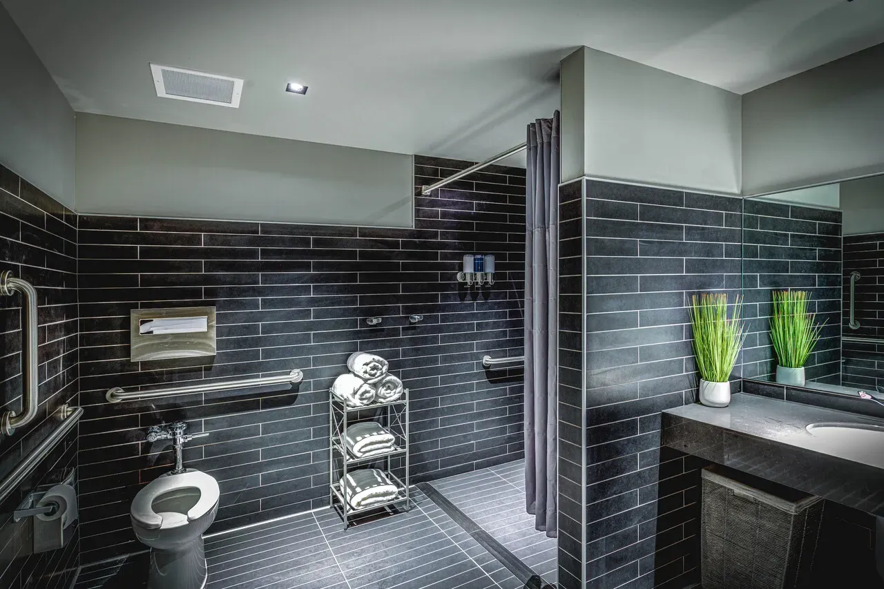 Restroom with dark tile walls, grab bars, a curtained shower and a sink.