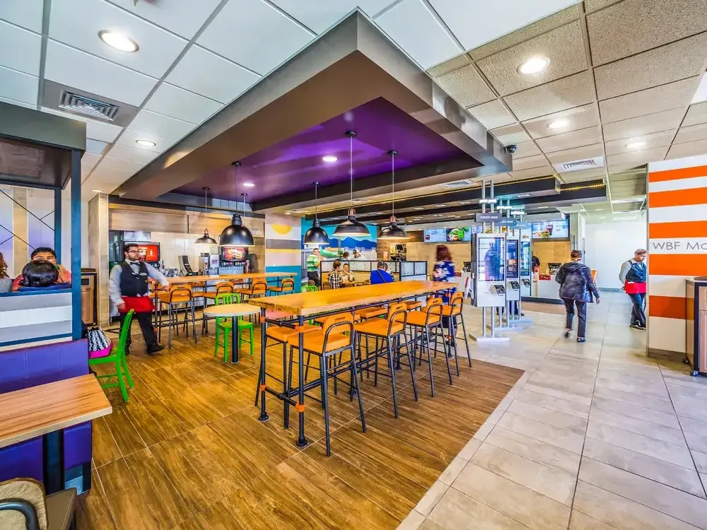 Wide view of the dining room with purple booths, a tall wood communal table and a lowered purple ceiling soffit.