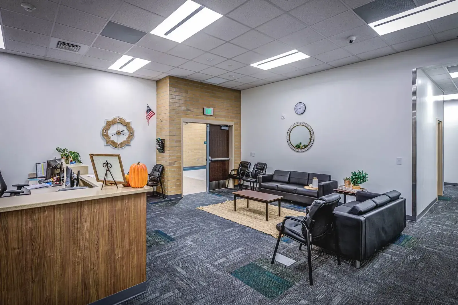 School office with a wood reception counter and a waiting area with black leather chairs and a sofa.