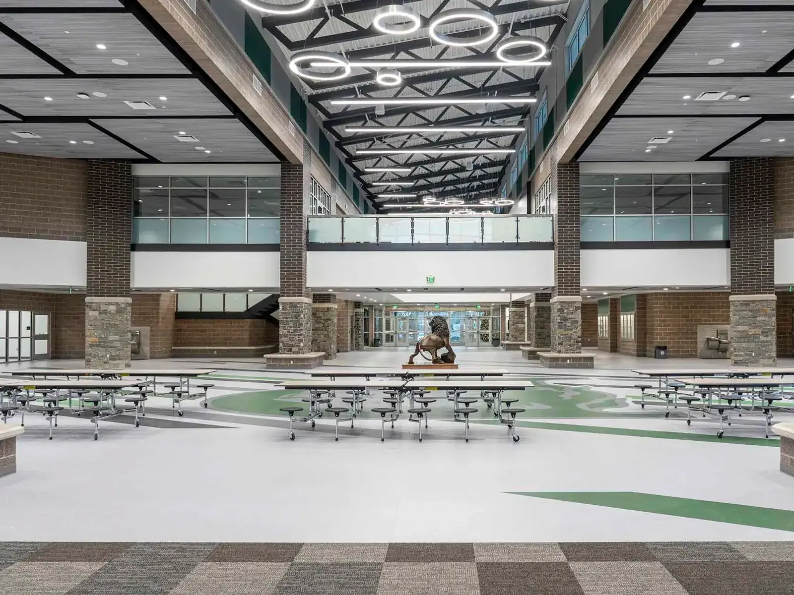 Wide commons with cafeteria tables, brick and stone columns and a lion statue in the distance