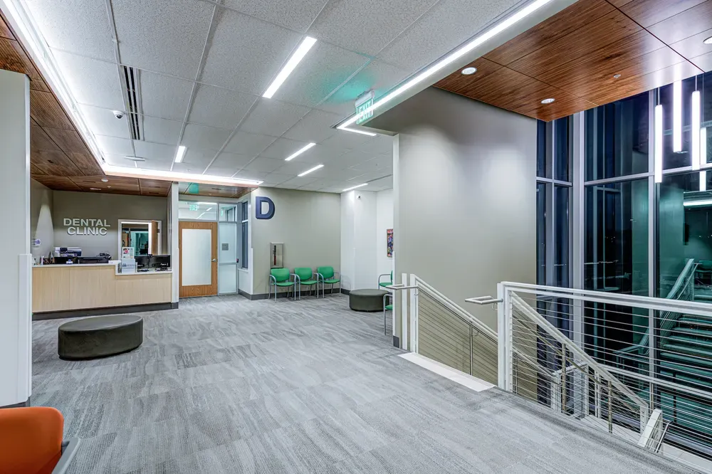 Dental clinic reception and waiting area beside a staircase with cable railings and a glass wall.