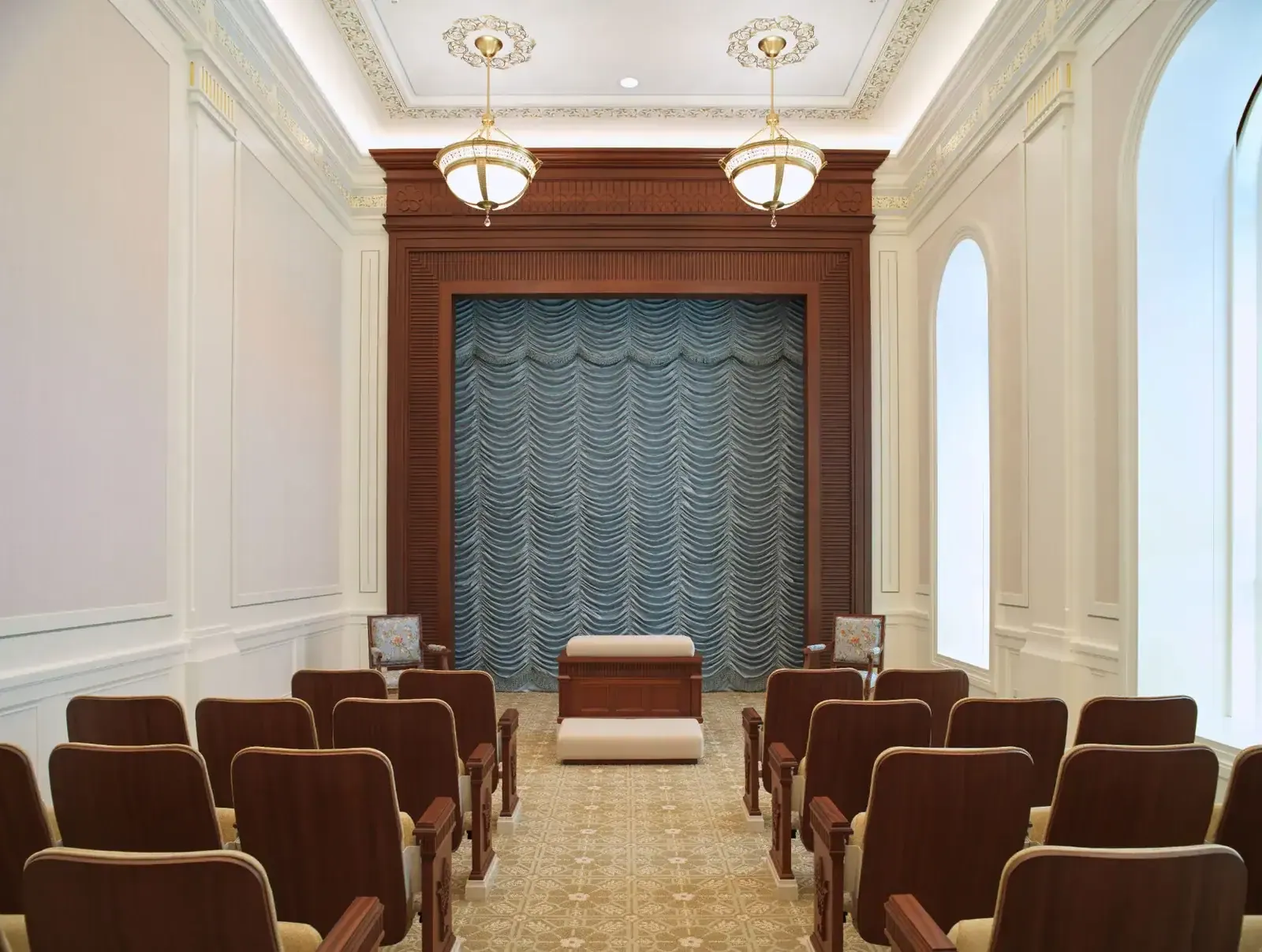 Instruction room with rows of wood-framed seats facing a draped blue curtain set in a carved wood frame