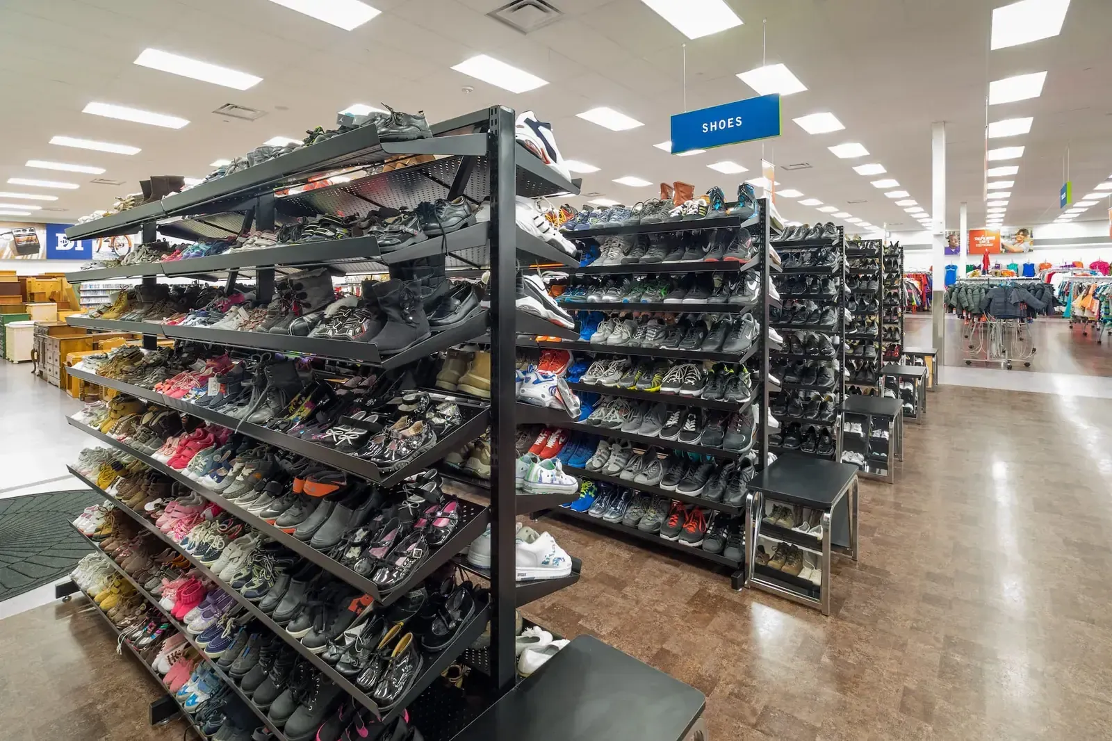 Shoe section with tiered racks of shoes and a blue Shoes sign overhead.