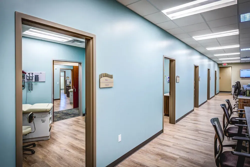 Corridor with teal walls, open exam room doors and a workstation at the far end.
