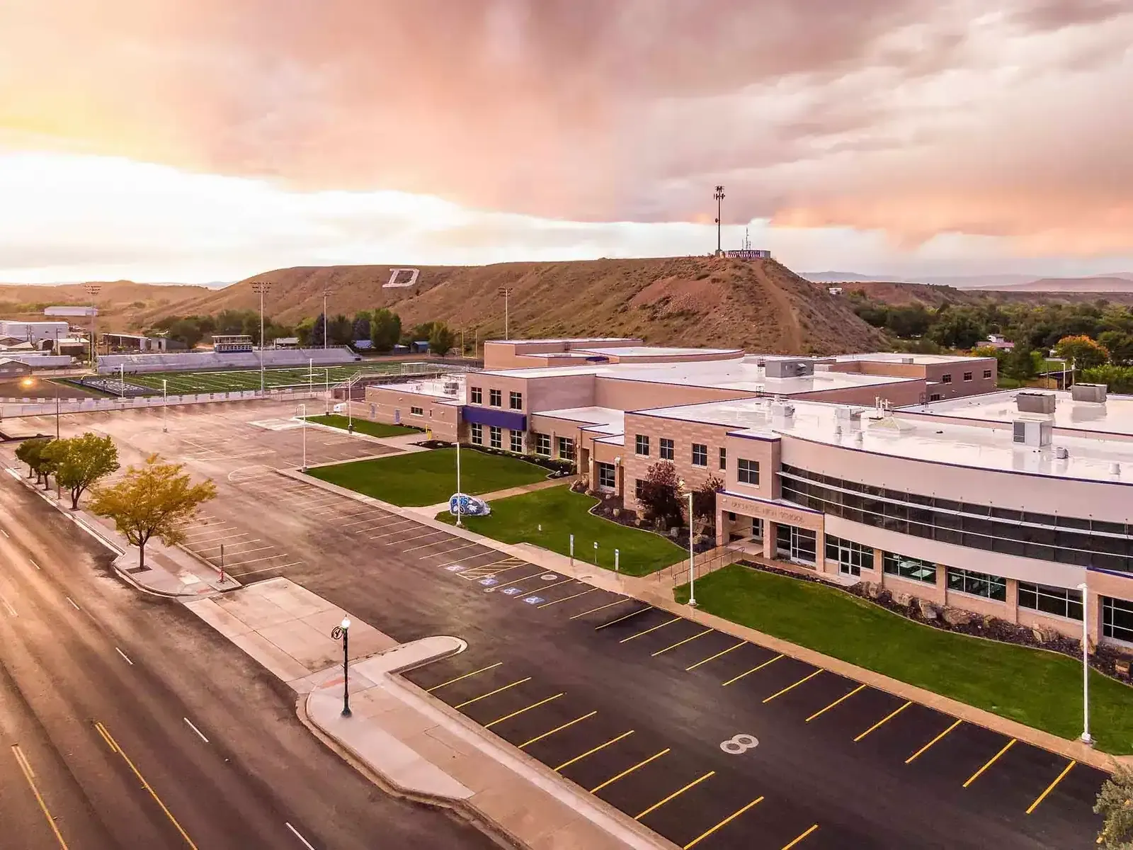 Aerial view of the school's main building and parking lot with the football field and hills beyond