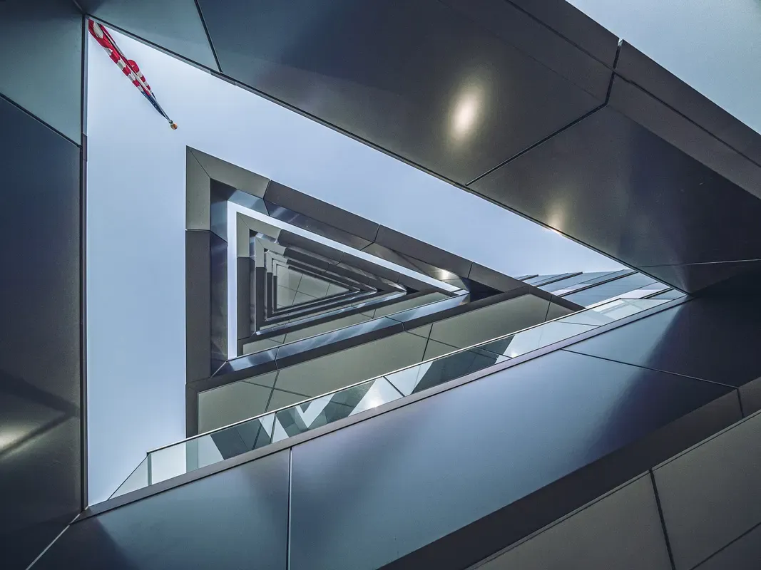 Upward view of a triangular stairwell opening framed by metal panels and glass railings