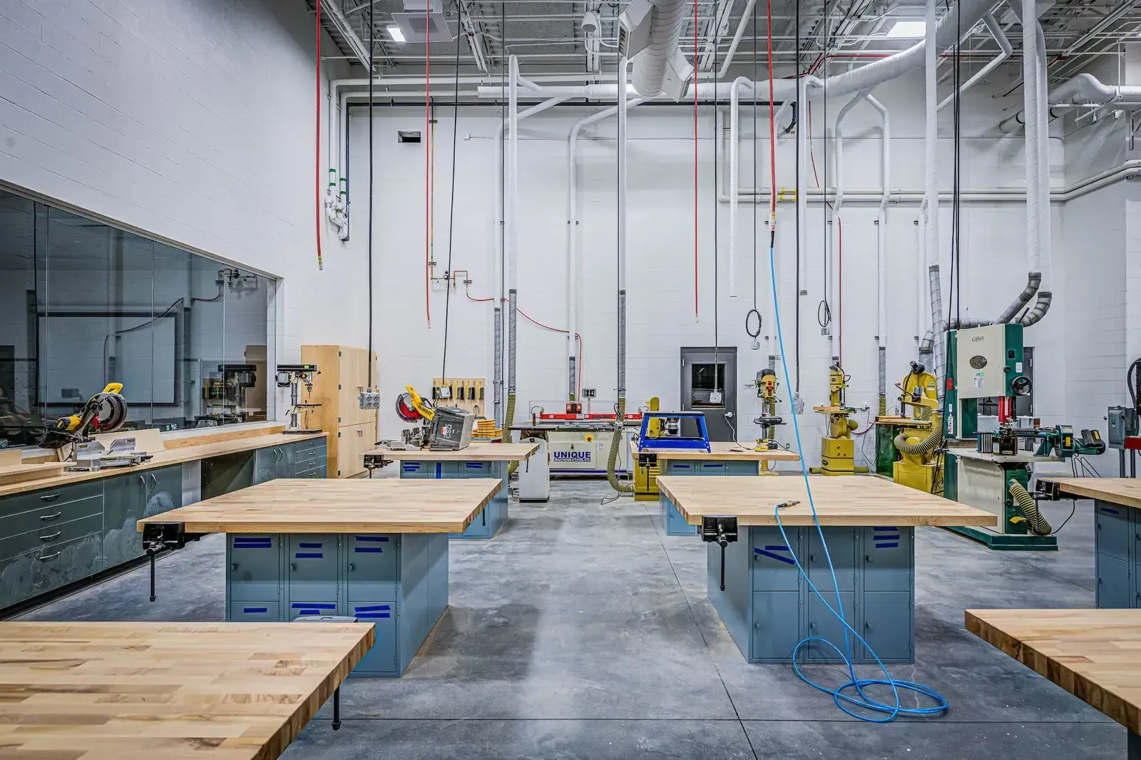 Shop classroom with butcher-block workbenches, machine tools and overhead dust collection ducts