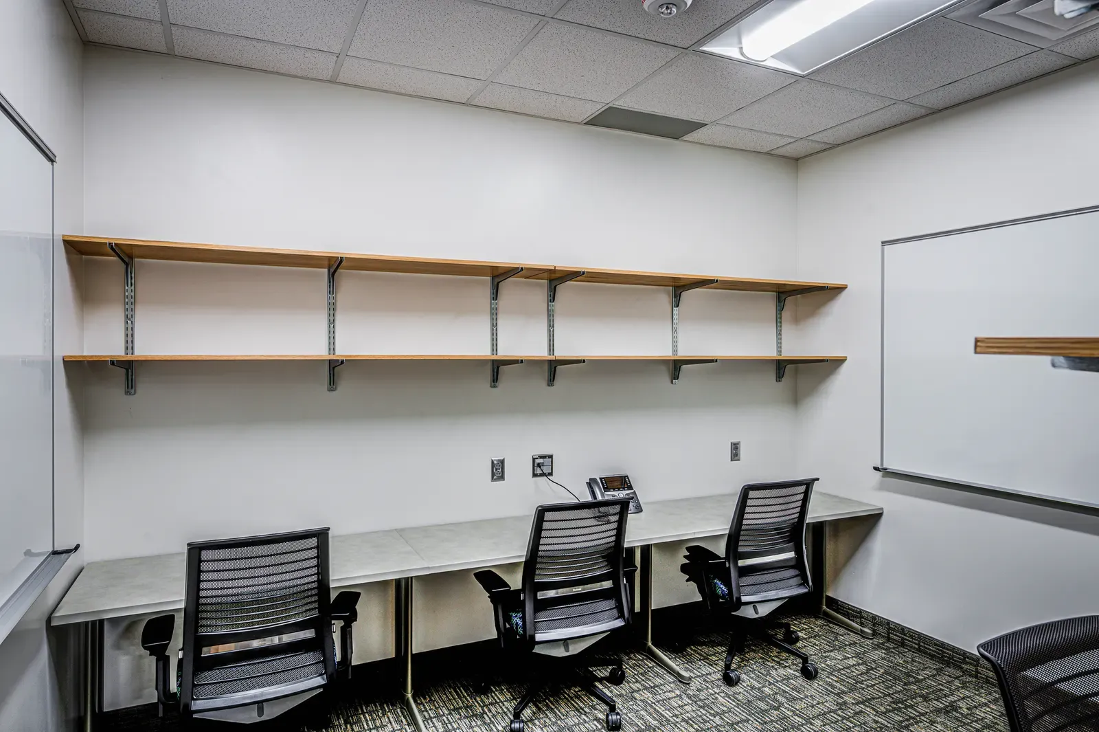 Small work room with open shelves and three desk chairs at a long counter