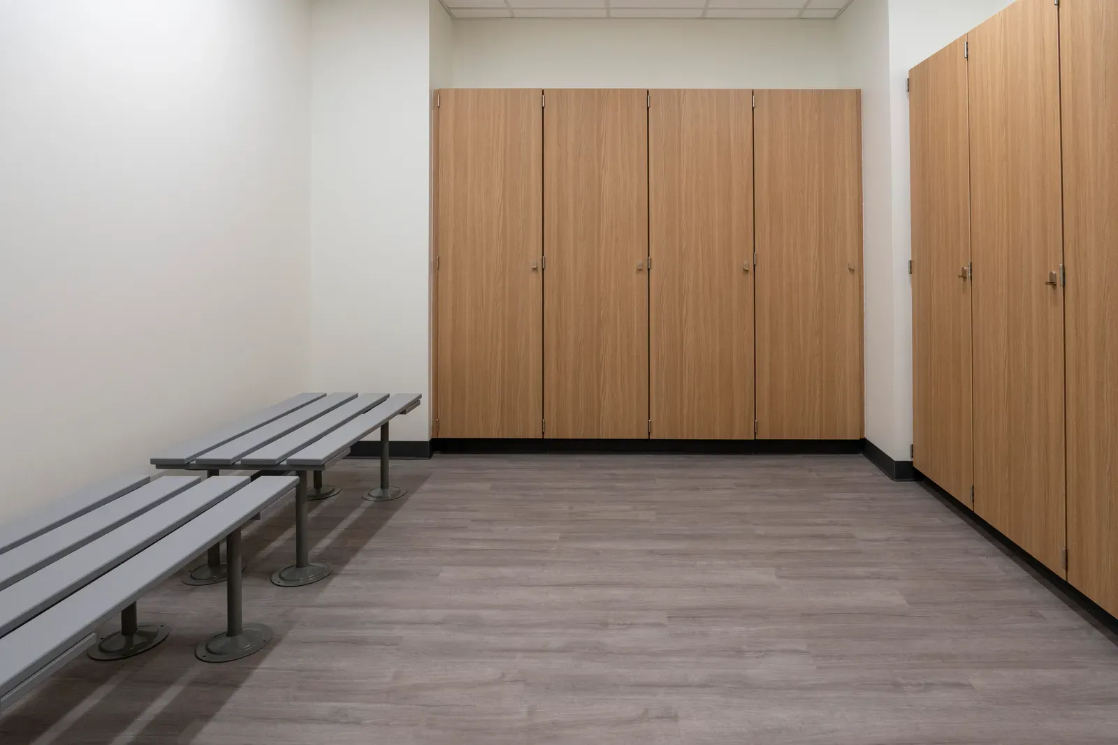 Locker room with wood-grain lockers and metal benches on a gray floor.