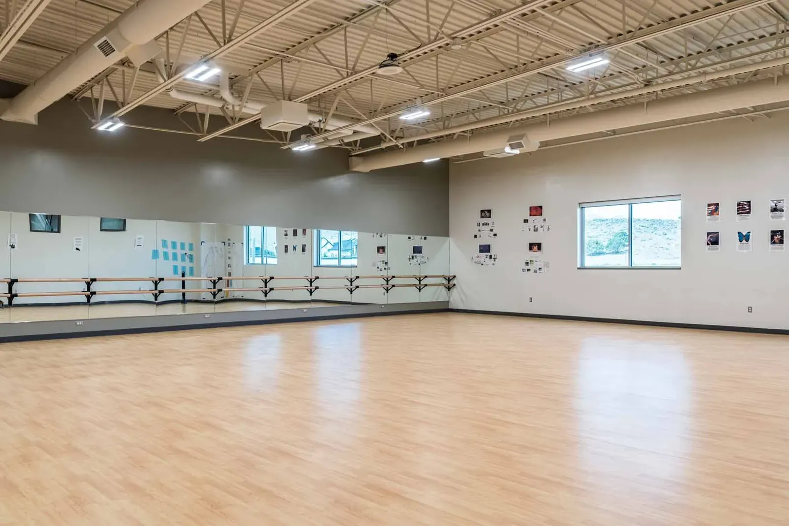 Dance studio with a wall of mirrors, ballet barres and a wood floor.