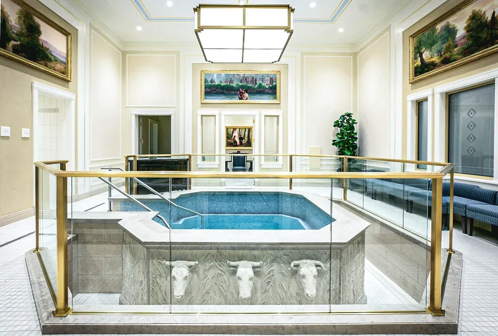 Baptismal font with carved oxen on its base, a gold railing and framed paintings on the walls behind.