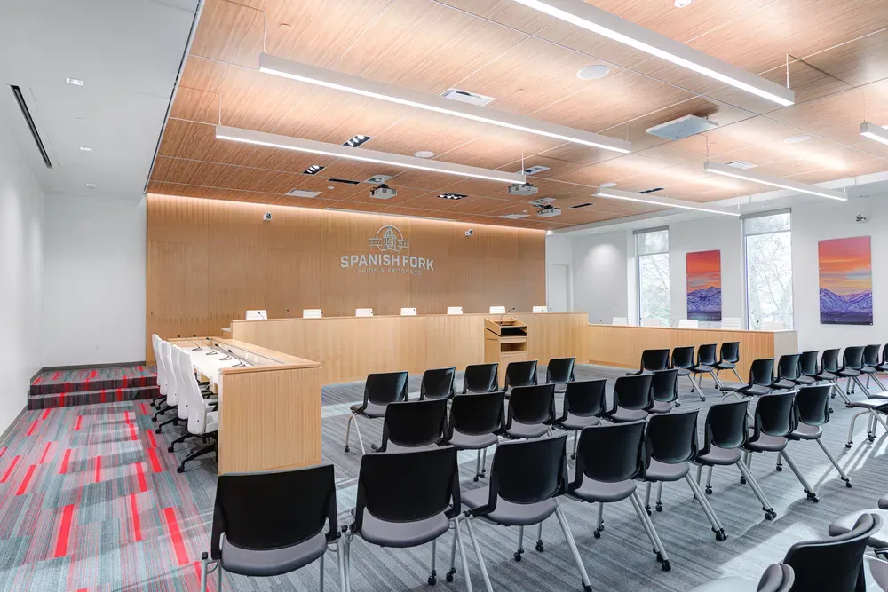 Council Chambers with a wood dais, the Spanish Fork logo on the wall, rows of black chairs and a wood-slat ceiling