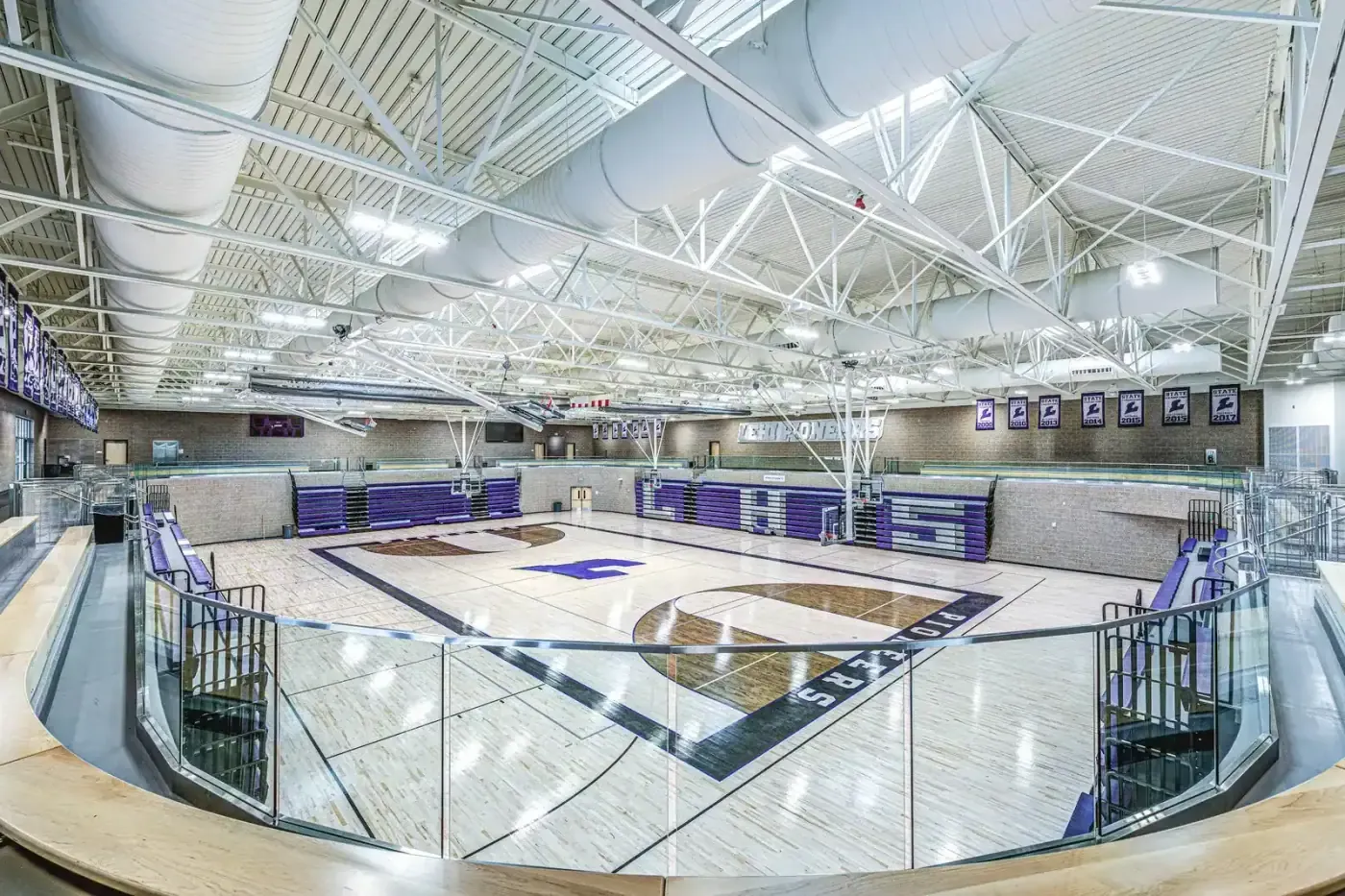 Gymnasium with a wood floor, purple bleachers and steel roof trusses.