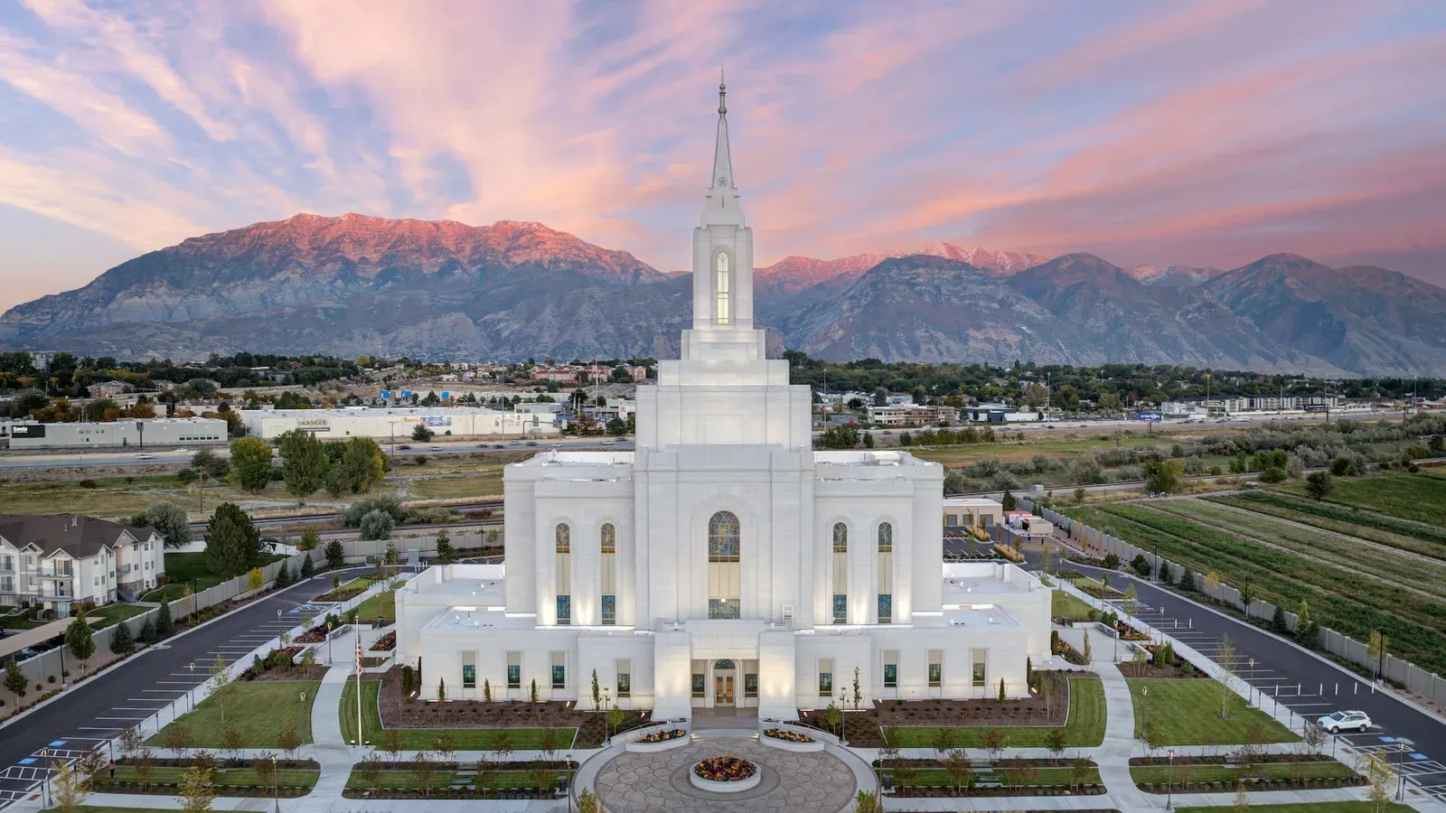 Aerial view of the lit temple facing its front plaza, with fields, roads, and mountains beyond.