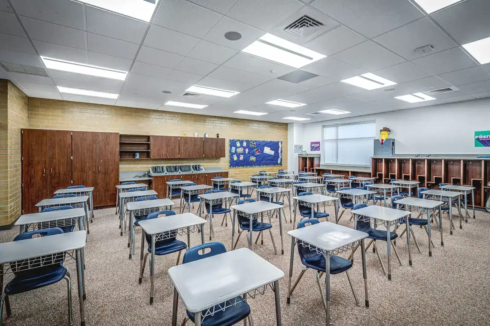 Classroom with rows of student desks and chairs, wood cabinets and a bulletin board.