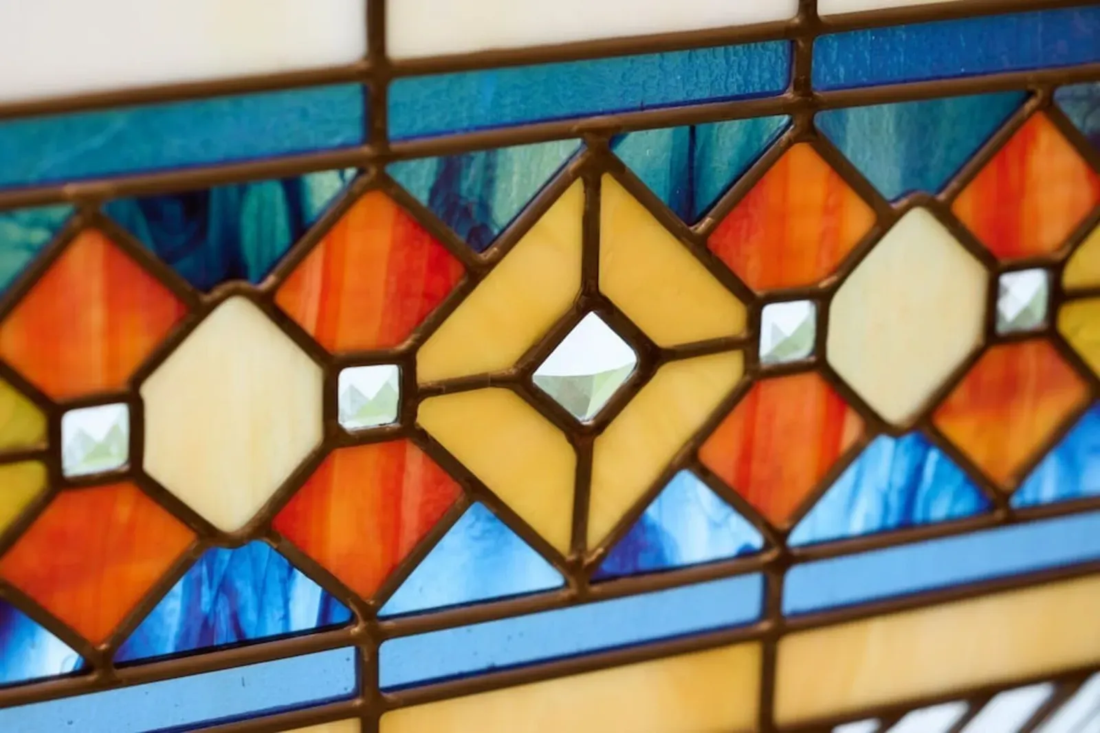 Close view of stained glass in orange, yellow and blue diamond patterns with clear beveled squares