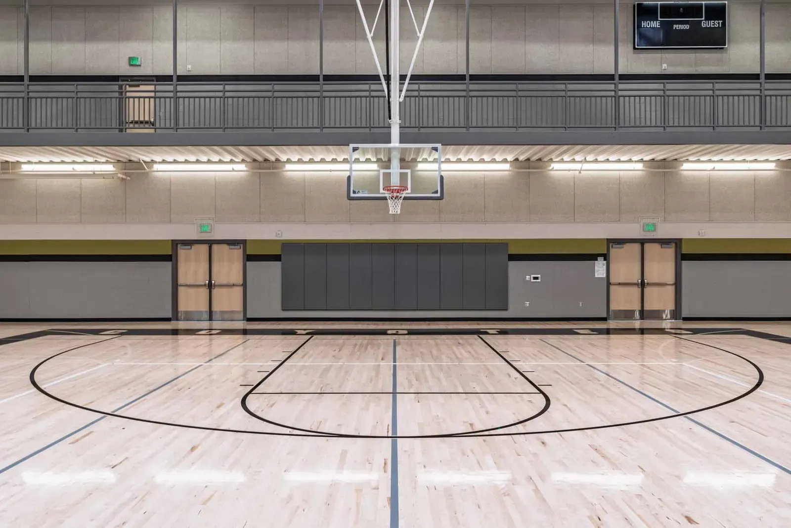 Gymnasium with a hardwood court, a basketball hoop and an upper walkway.
