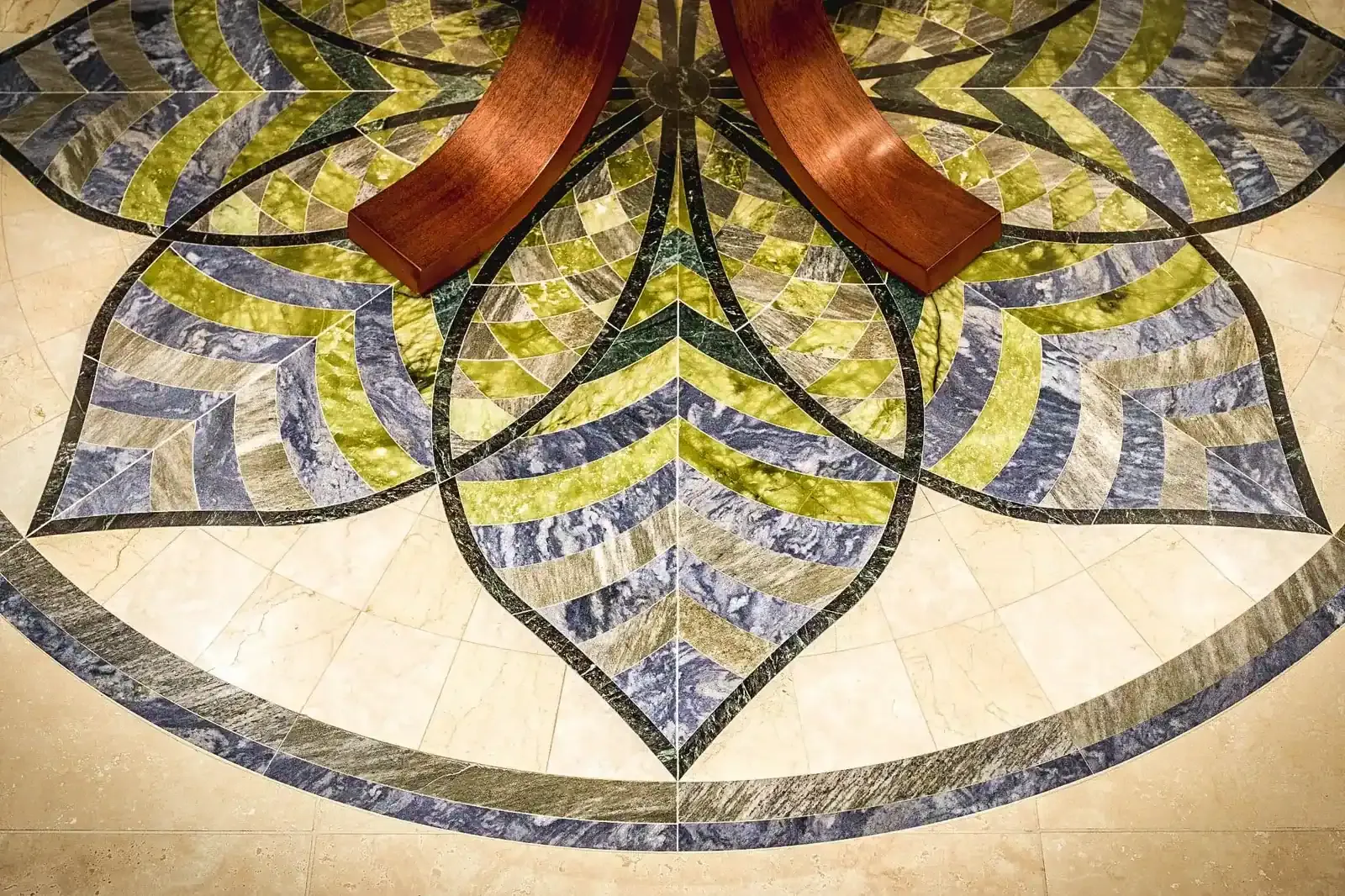 Flower-shaped marble floor inlay in blue, green, and gold stone beneath a wood table.