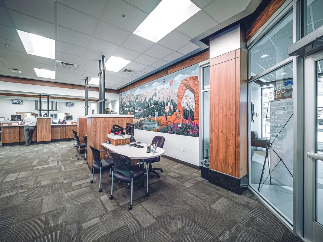Branch lobby with wood-paneled teller counters, a small round table and a landscape mural beside a glass door