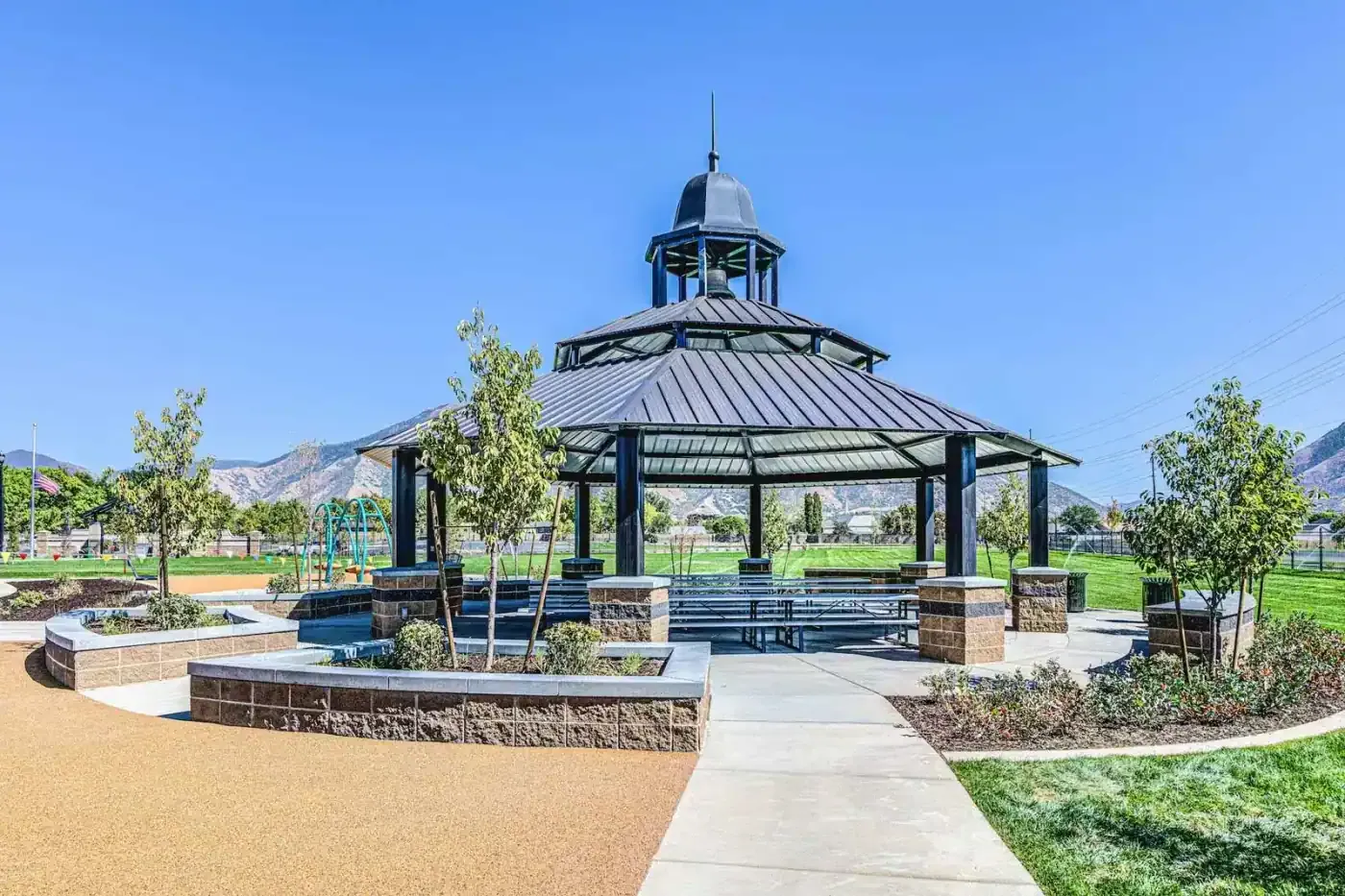 Octagonal metal-roofed pavilion with picnic tables, stone-faced planters and a rubberized walkway