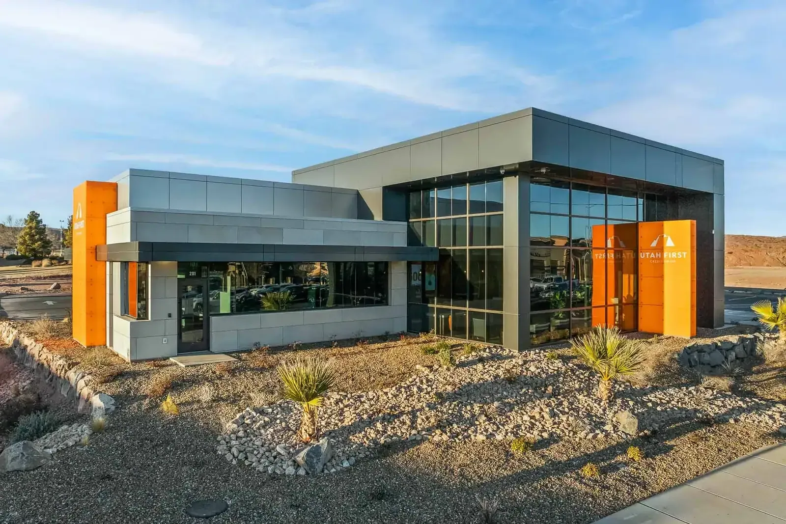 Daytime view of the branch with gray metal panels, orange accent panels, a glass curtain wall and desert landscaping.