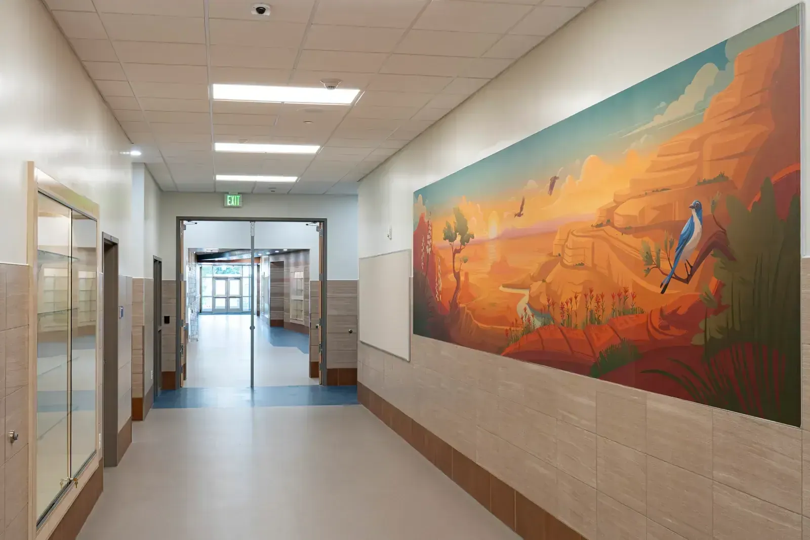 Hallway with a large mural of a bluebird in a red rock canyon, beside a glass display case.