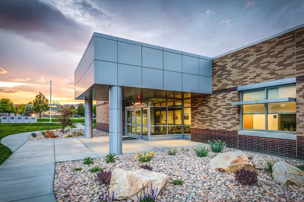 Side entrance with a metal-panel canopy, brick walls and rock landscaping at sunset.