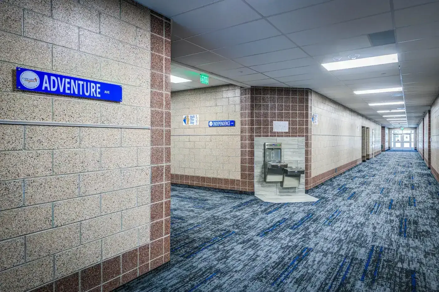 Corridor with blue patterned carpet, an Adventure classroom sign and a drinking fountain alcove.