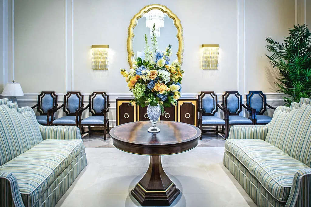 Sitting area with a round wood table holding flowers, striped sofas, a gold mirror and wall sconces.