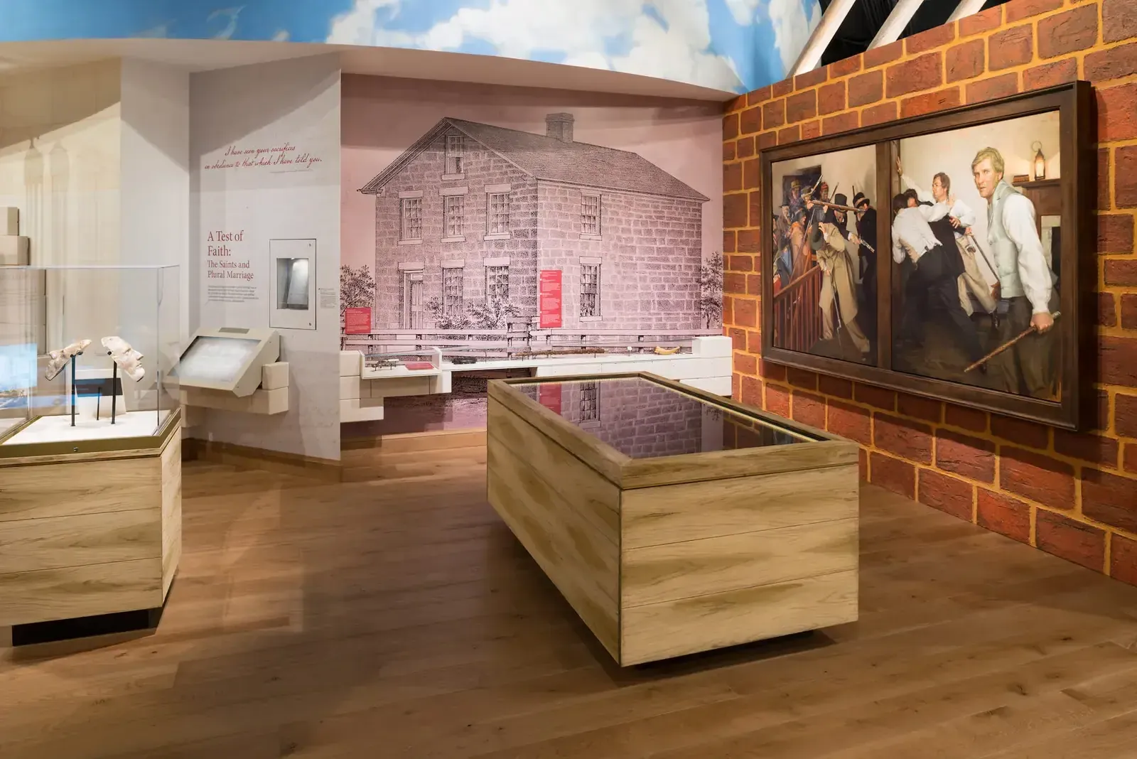 Exhibit with a mural of a stone house, a wood display table, and a painting on a brick wall