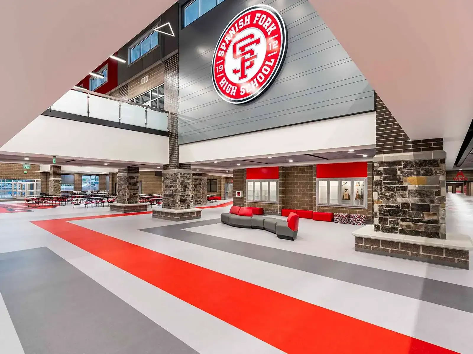Commons with a red stripe across the gray floor, lounge seating, stone columns, and the school seal on the wall.