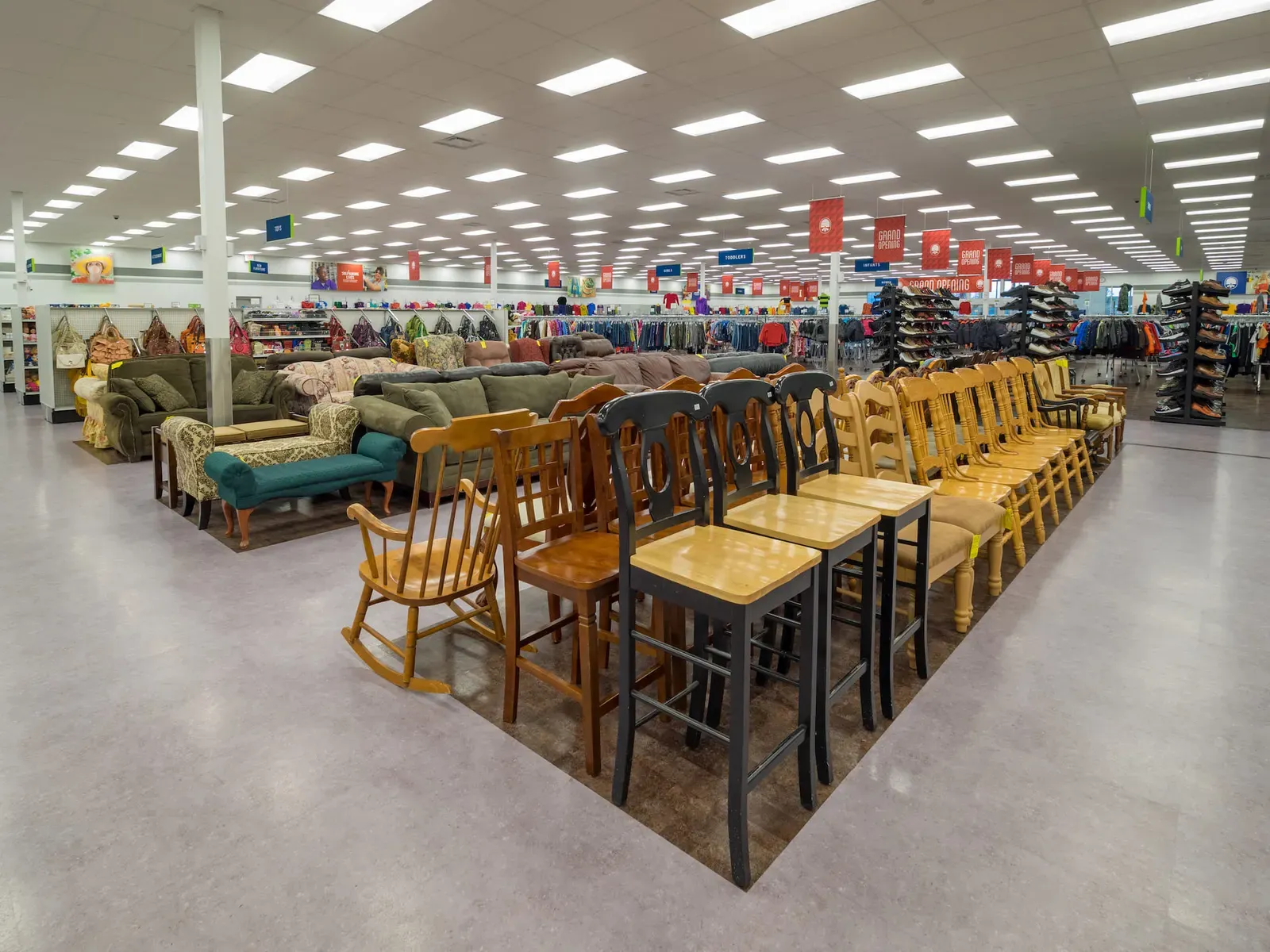 Furniture area with rows of wooden chairs and sofas in front and clothing racks beyond.