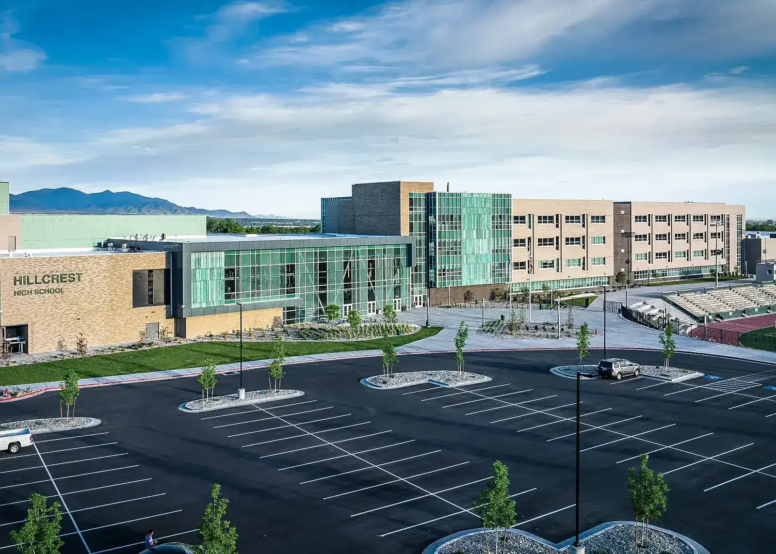 School entrance and glass-walled wing seen across the parking lot, with a Hillcrest High School sign at left