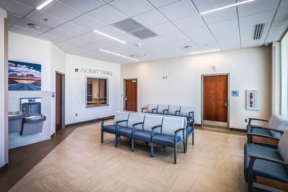 Admitting waiting area with a row of blue chairs, a drinking fountain and a landscape photo on the wall