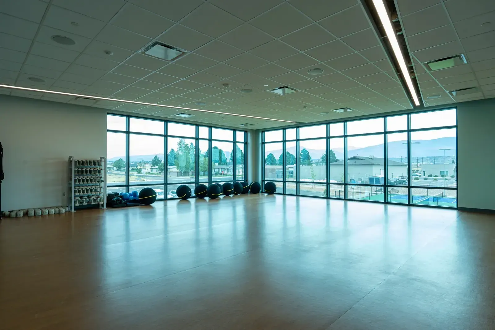 Group exercise room with a wood floor, a wall of windows, exercise balls and a weight rack.