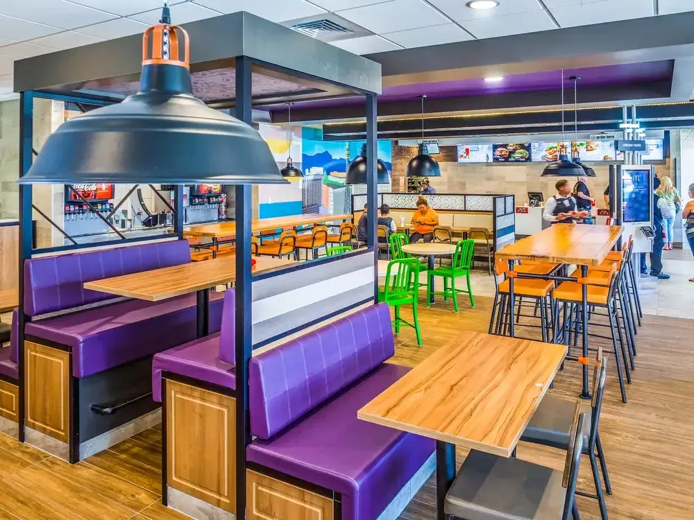 Purple booth seating and tall tables beneath large industrial pendant lamps.
