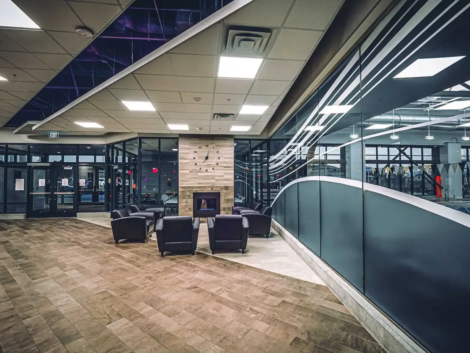 Wide view of the lobby lounge with chairs around a fireplace and a curved glass wall at right.