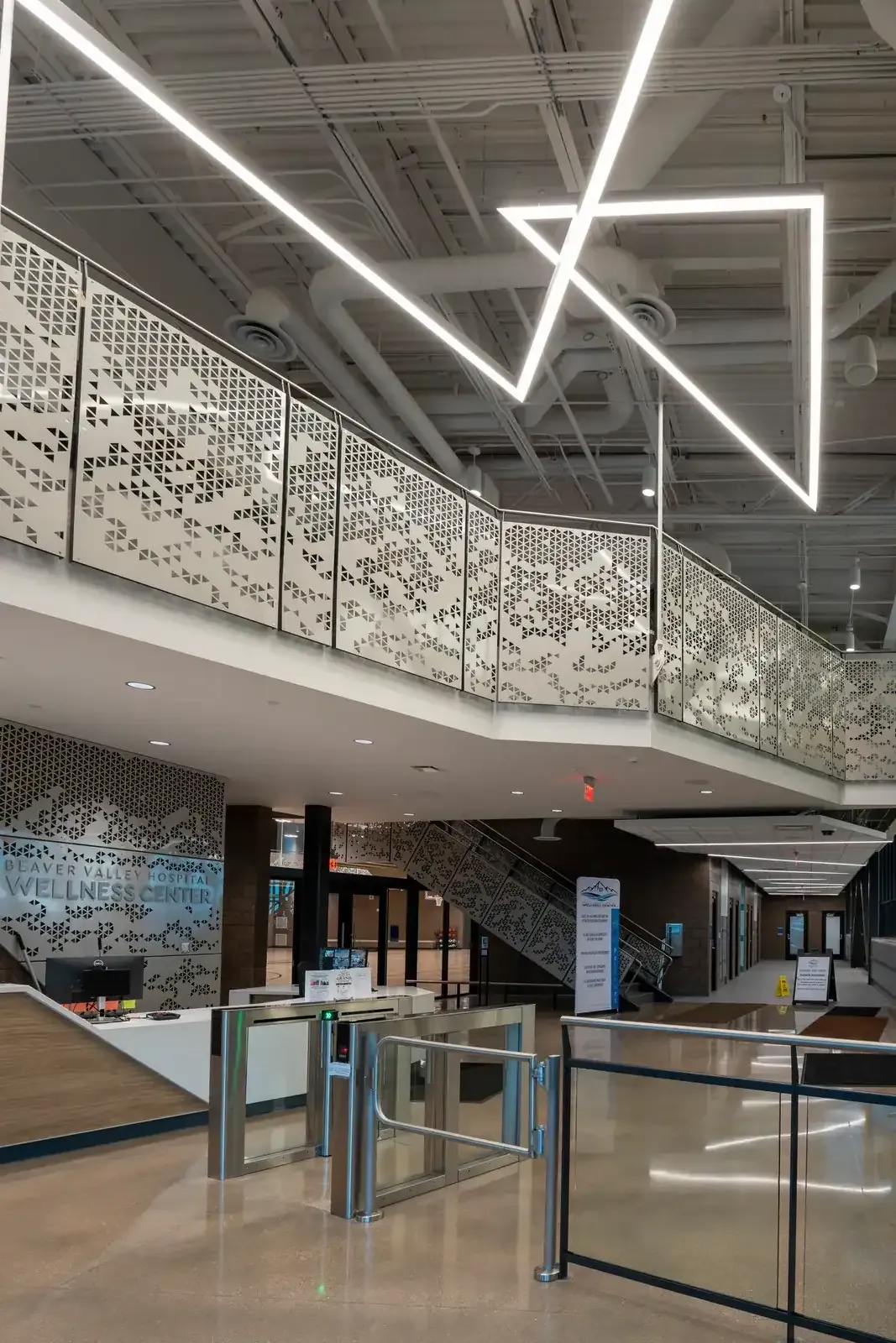 Lobby with a reception counter and Wellness Center wall sign, a stair with perforated metal railings and a star-shaped light fixture overhead.