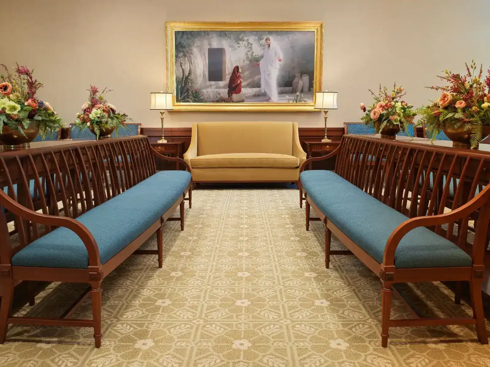 Hall with two upholstered wood benches facing a gold-framed painting, a settee and flower arrangements