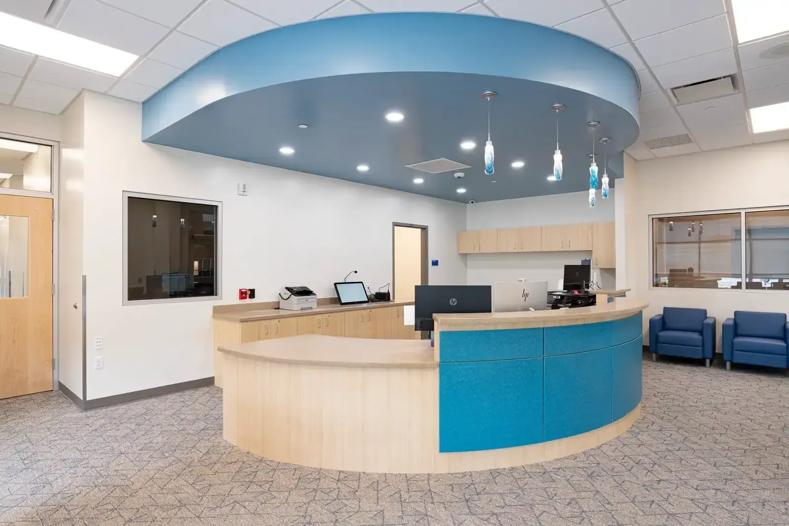 Front office with a curved wood and blue counter, a blue ceiling soffit and two blue chairs.