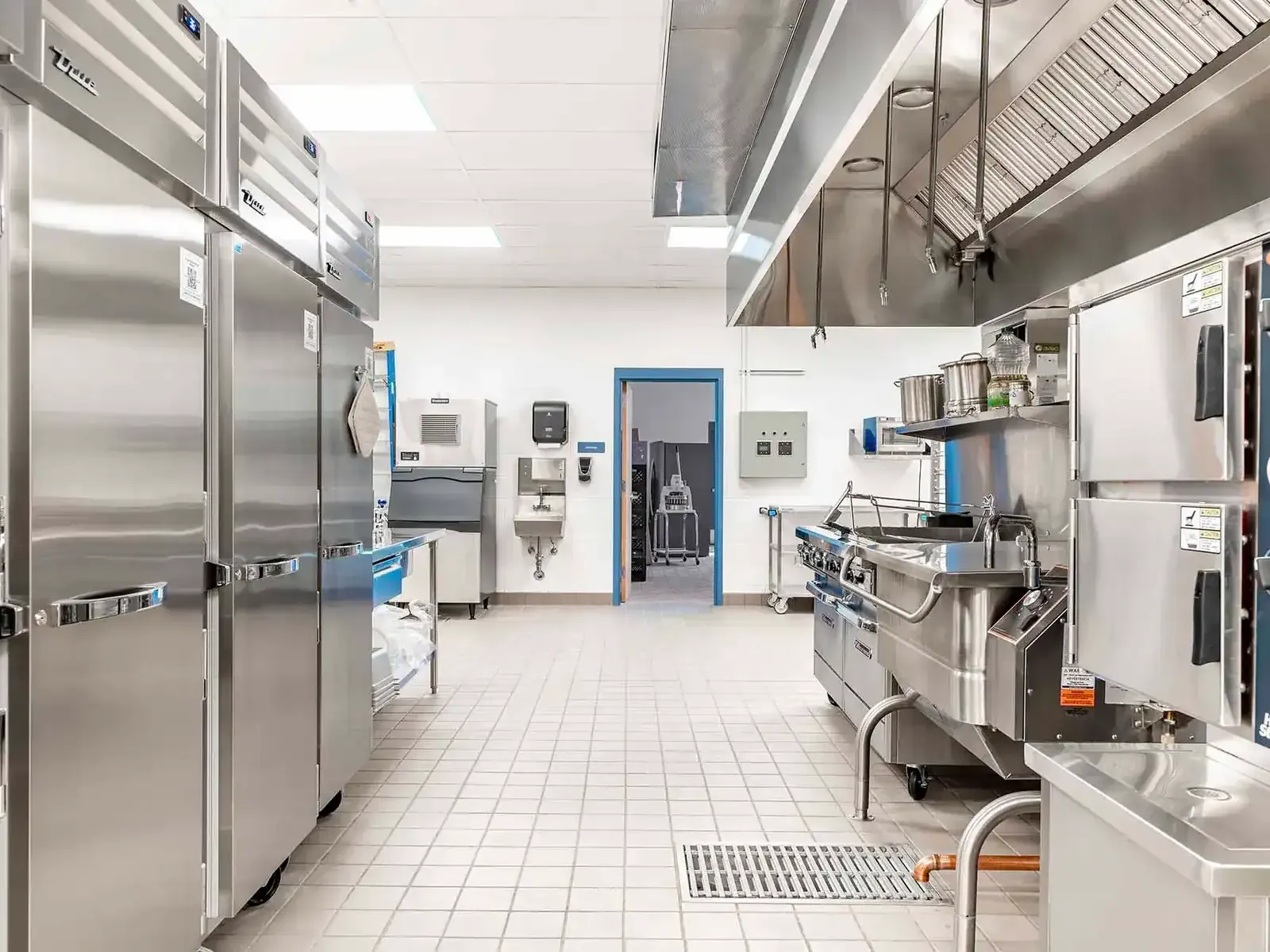 Commercial kitchen with stainless-steel refrigerators, cooking equipment, and an exhaust hood