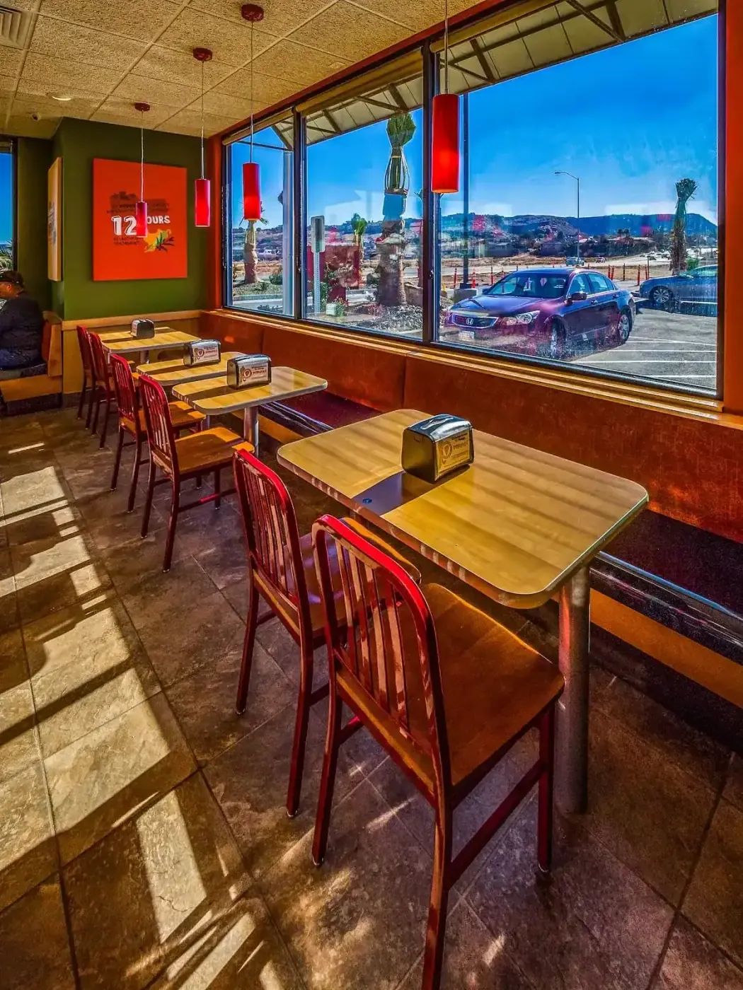Window-side tables with red chairs facing the parking lot.
