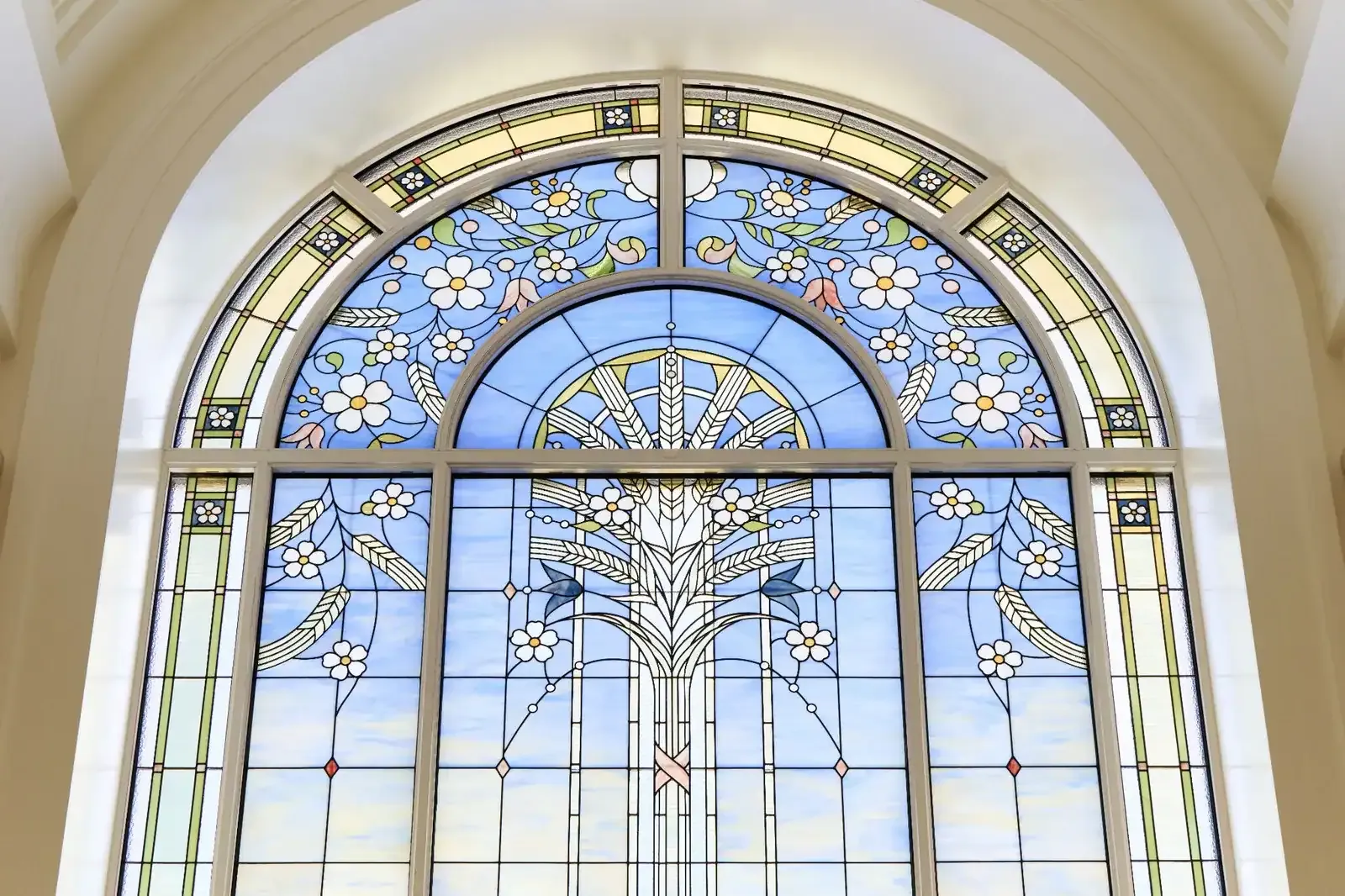 Arched stained-glass window with a wheat motif, white flowers and a blue sky background