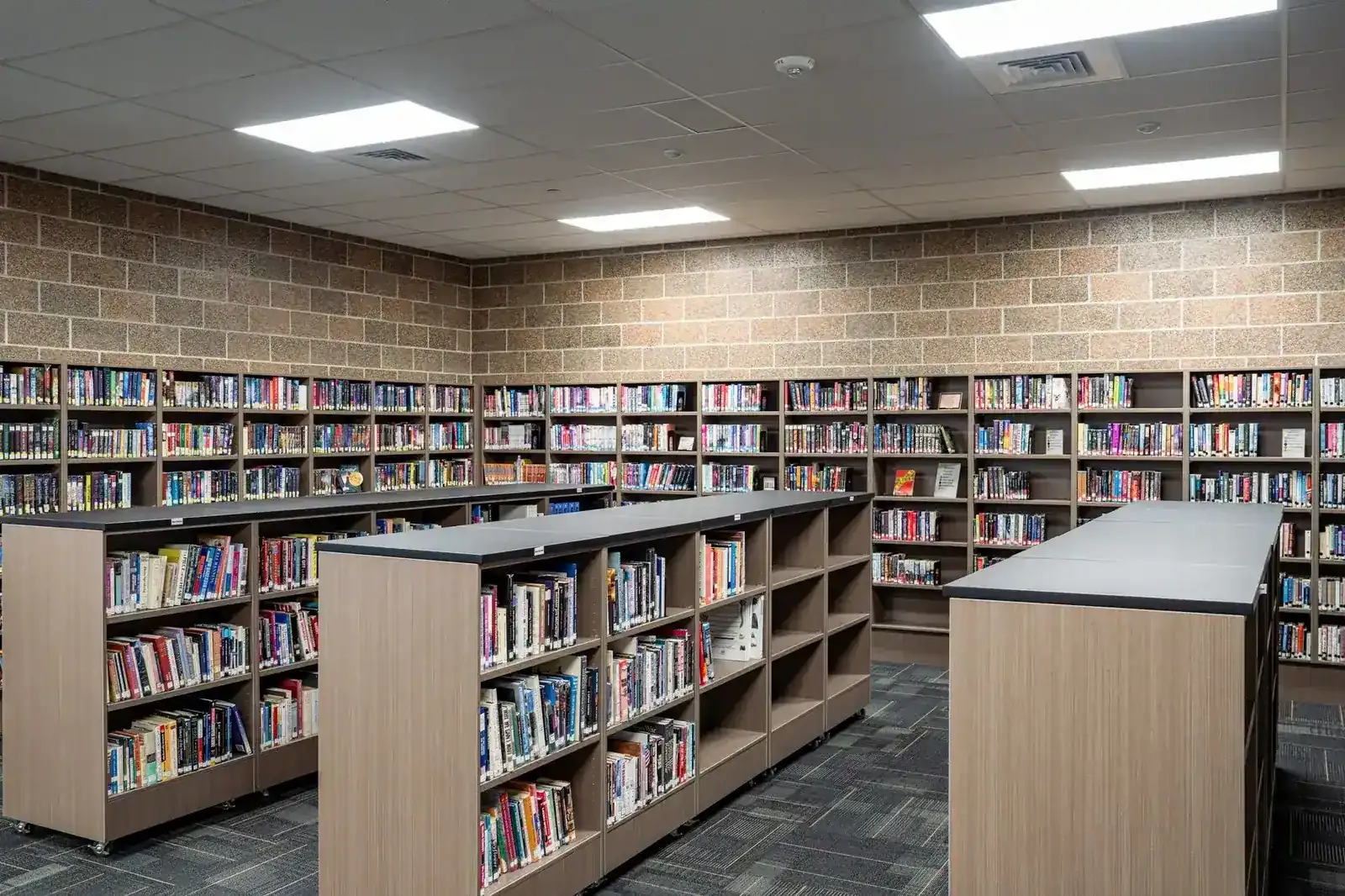 Library with wood and black bookshelves, mobile shelving units and a concrete block wall.