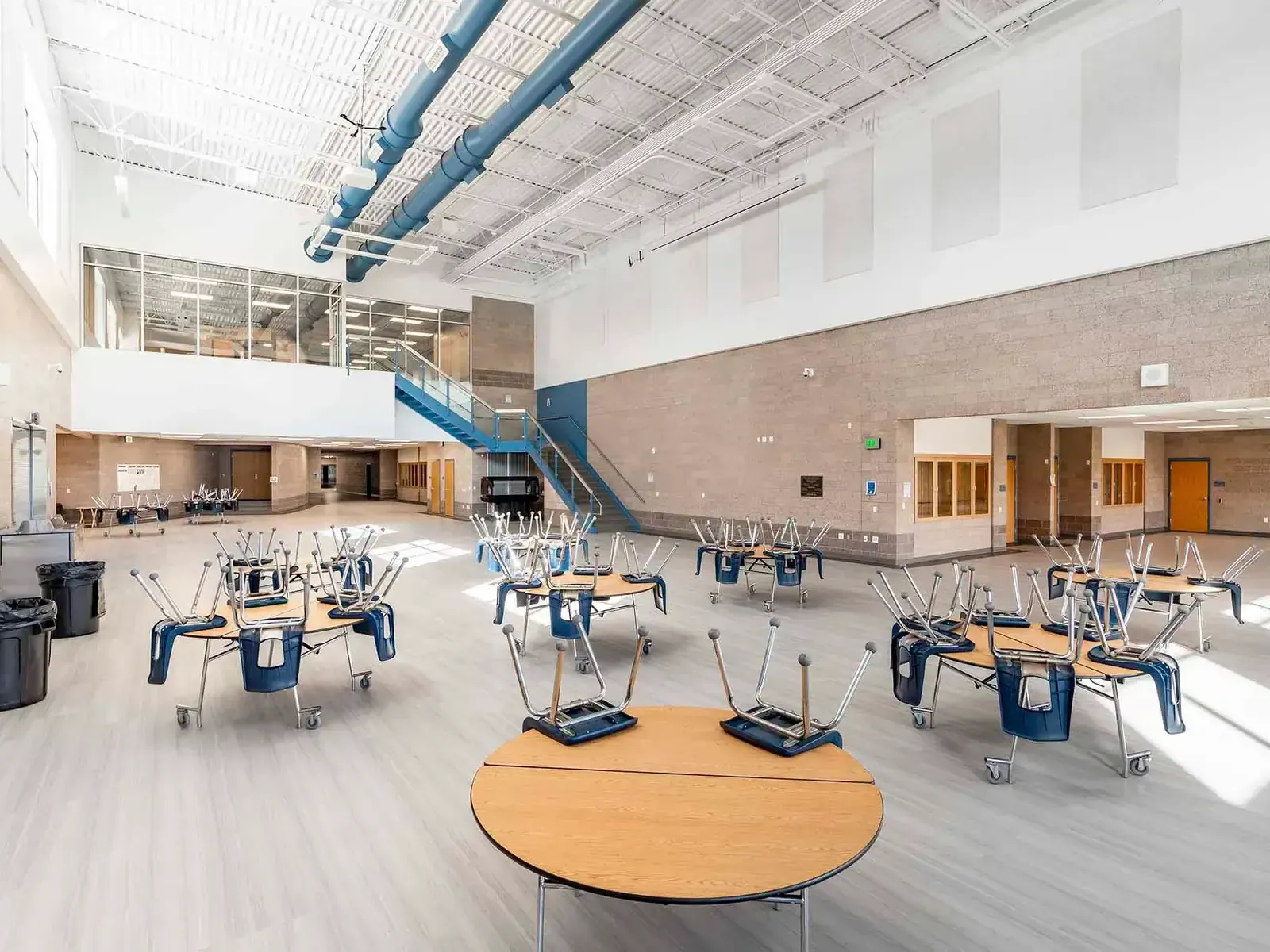 Two-story commons with round tables, a blue staircase, and a mezzanine overlooking the dining area