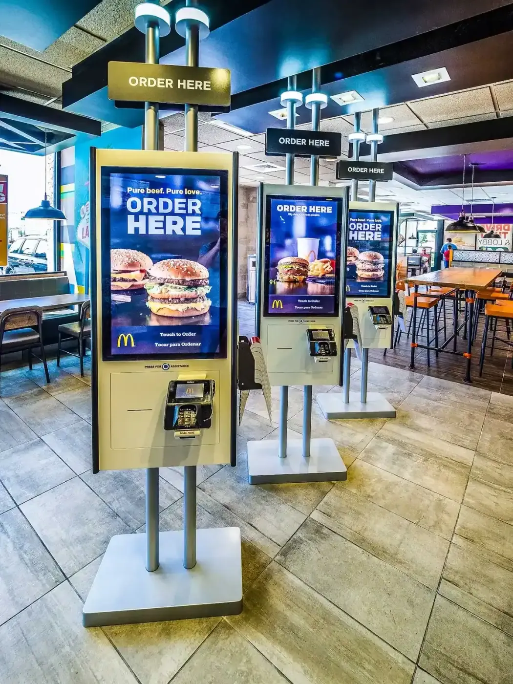 Three self-order kiosks on stands in the dining room.